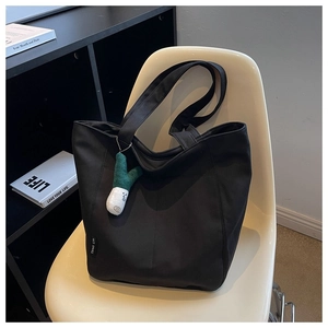 Close-up of black canvas tote bag with brand label and cute plush charm on a chair