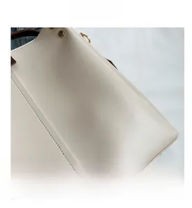 Detail view of cream faux leather bag texture with brown canvas strap and gold buckle