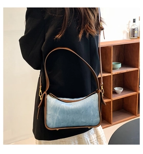 Detail of vintage-style blue shoulder bag with brown leather straps and gold hardware