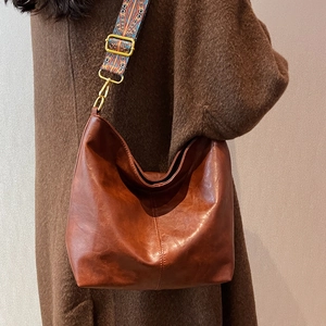 Retro brown leather bucket bag with bohemian printed wide strap worn by a model