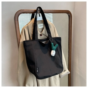 Detail of black canvas tote bag featuring an embroidered tag and green cactus plush charm