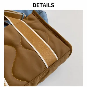 Detalle del bolso tote de nailon acolchado marrón con costuras onduladas y correa a rayas