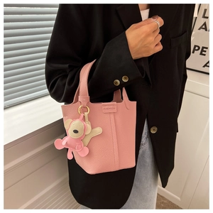Rosafarbene Eimertasche aus Leder mit Kieselstruktur und Affenanhänger am Model