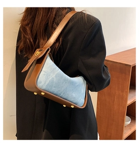 Detailed back view of a blue denim and brown leather crescent shoulder bag with metal studs