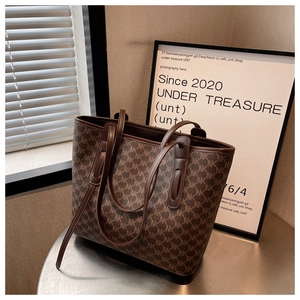 Detail of the brown monogram tote bag on a metal table showing the handle and texture