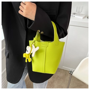 Detail der neongrünen Beuteltasche aus Leder mit Modeplakette und Anhängern