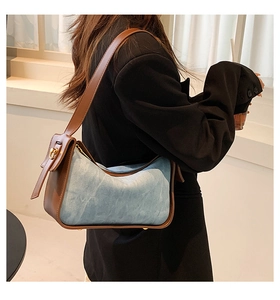 Detail of blue denim and brown leather stitching on underarm bag with gold buckle