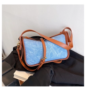 Close-up of blue denim crossbody bag with brown leather trim and golden metal hardware