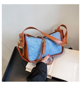 Detail of denim shoulder bag with brown leather trim and golden metal buckle close-up