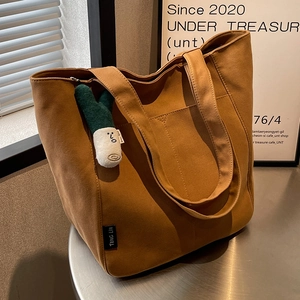 Caramel canvas tote bag for women with green plush charm on silver metal surface