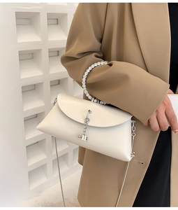 Detail of cream crossbody bag with rhinestone-encrusted round handle and silver chain