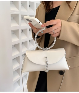 Close-up of white leather handbag featuring a crystal-embellished circular handle and chain