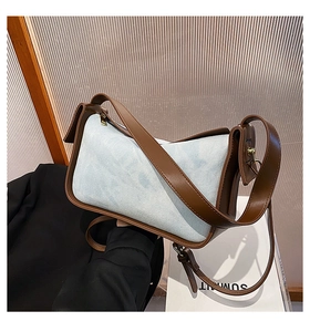 Detail of retro denim and brown leather shoulder bag with golden hardware on a white box