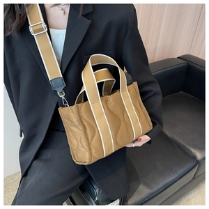 Detalle de bolso tote de nailon acolchado marrón con correa ancha en sofá negro
