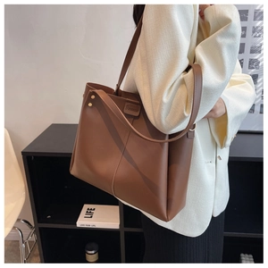 Brown leather tote bag detail with decorative gold rivets shown with a white blazer outfit