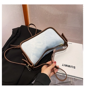 Detail of light blue denim shoulder bag with brown leather trim and golden zipper