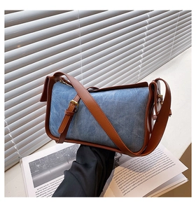 Detail of blue denim shoulder bag with brown leather trim and adjustable strap