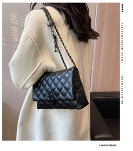 Side view of black quilted crossbody bag with gold metal chain and ball charm on model