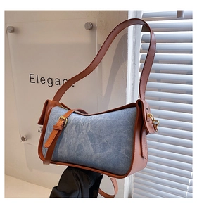 Detail of blue denim shoulder bag with brown leather trim and metallic side buckle accents