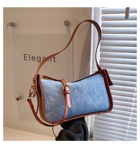Close-up of blue denim shoulder bag featuring brown leather trim and gold-tone hardware