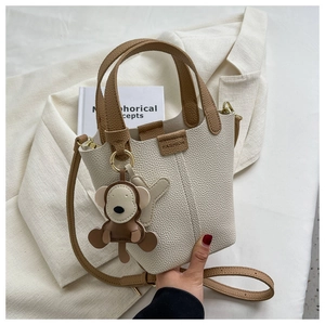 Detail der beigen Beuteltasche mit braunen Griffen und Affenanhänger auf weißem Blazer