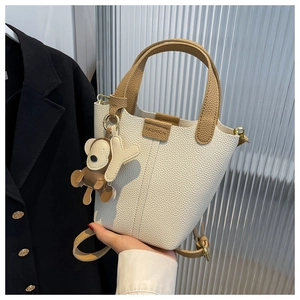 Detail der beigen Beuteltasche aus Leder mit Lychee-Muster, Mode-Label und Affen-Anhänger