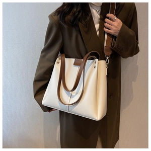 Detail of white tote bag with brown handles, metal studs, and wide fabric strap