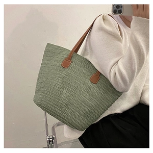 Detailed close-up of a large green woven straw tote bag with brown leather shoulder straps