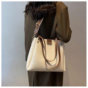 Detail of a large beige tote bag with brown wide strap worn on a gray suit