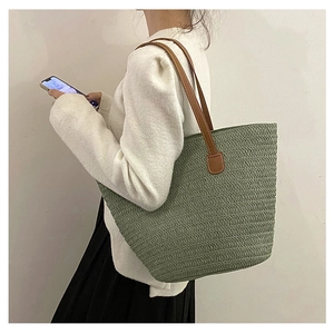 Detail of sage green woven straw tote bag featuring brown leather straps on a model