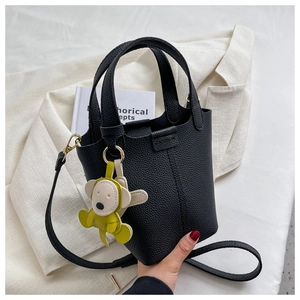 Schwarze Eimer-Handtasche aus Leder mit Mode-Logo und Affen-Anhänger auf weißem Sakko