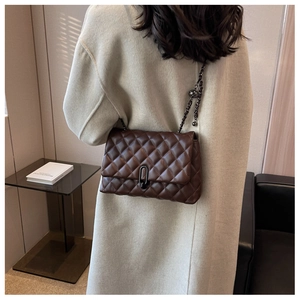 Detail of dark brown quilted leather bag with metallic chain and oval buckle on model