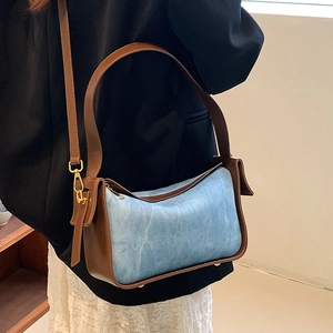 Blue textured shoulder bag with brown leather trim shown on a stylish model