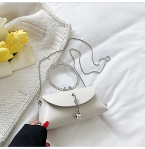 Macro shot of white crossbody bag featuring a crystal-encrusted ring handle and metal chain