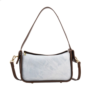Blue denim and brown leather patchwork underarm bag with gold hardware on white background