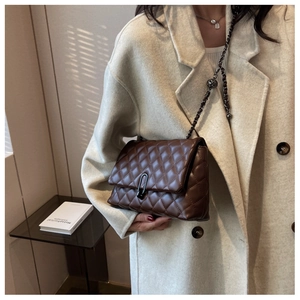 Close-up of quilted dark brown leather bag with chunky black metal chain and U-buckle