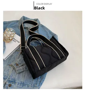 Detalle de bolso tote acolchado de nailon negro con correa ancha sobre denim