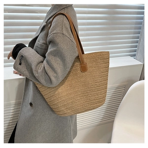 Detail view of the woven straw tote bag texture with brown leather shoulder straps