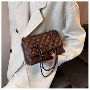 Detail of a brown quilted leather shoulder bag with dark metal chain strap and unique clasp