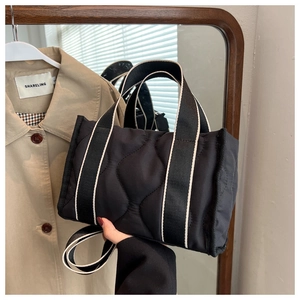 Detalle de bolso tote de nailon negro acolchado con correas a rayas y textura