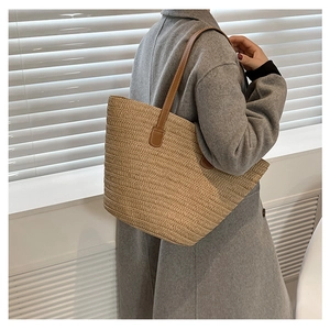 Detail of handwoven straw tote bag with brown leather shoulder straps worn by model