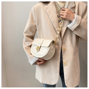 Detail of cream saddle bag with crocodile texture, gold lock, and acrylic chain strap
