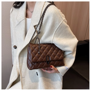 Detail of brown quilted leather bag with dark metal chain and round decorative ball charm