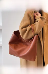 Close-up of a large caramel lychee leather tote bag worn by a model over a camel coat