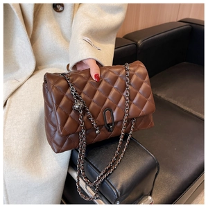 Detail of quilted dark brown chain bag with metallic ball charm on leather sofa