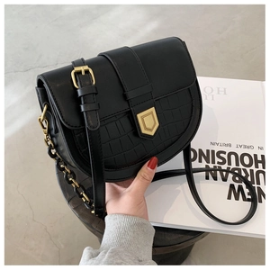 Close-up of black saddle bag with crocodile texture, gold shield lock and chain strap