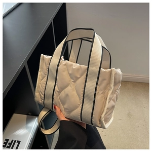 Detalle de bolso tote de nailon acolchado beige con ribete negro y correa ancha