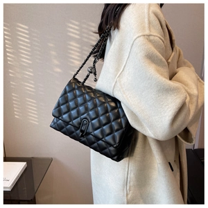 Detail of a black quilted chain bag with matte hardware worn over the shoulder