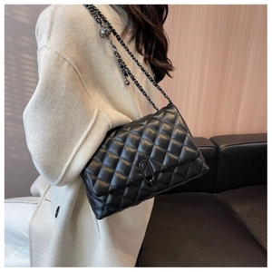 Detail view of black quilted leather bag with dark chain strap worn by a model