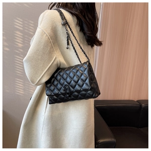 Detail of classic black quilted chain bag with sleek metal strap and round pendant charm